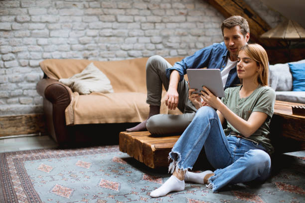 istock Happy couple using digital tablet while sitting  together oh the floor 1210350197