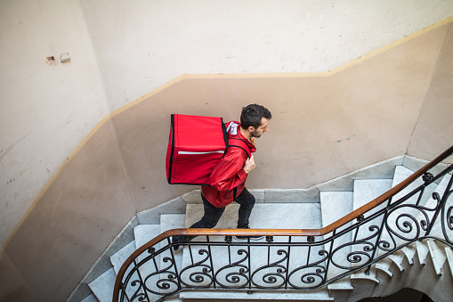 High angle view of male delivery worker moving up on steps in residential building on his way to customer