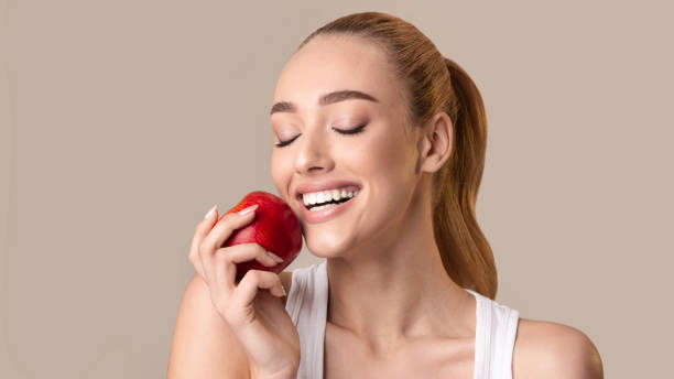 istock Woman Biting Red Apple Posing Standing Over Beige Background 1210351319