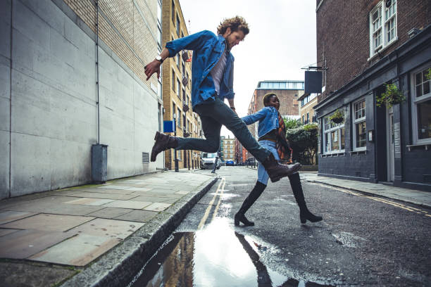 Young couple jumping a puddle after the storm