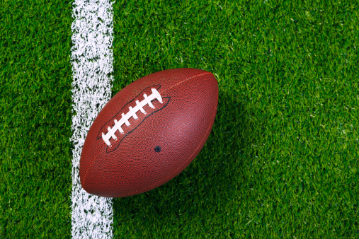A low angle view of a leather American Football inches from the white goal line of a red end zone.