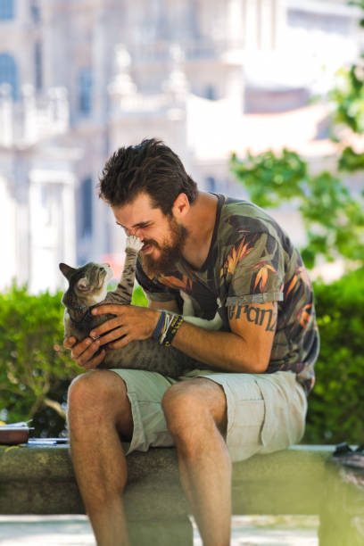 istock Young Man Playing With A Cat In Public Park 1210355963