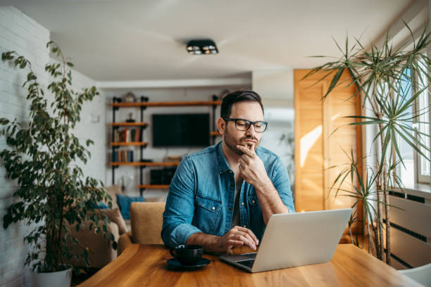 portrait of a puzzled man looking at laptop at modern home. - problems imagens e fotografias de stock