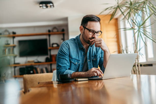 istock Pensive man looking at laptop while sitting at wooden table, portrait. 1210359011