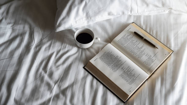 istock Alarm clock, book, cup of coffee and accessories on white bedding sheets with copy space. Morning lifestyle concept. 1210363046