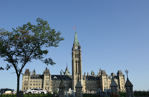 Ottawa, Canada - August 25, 2019: The Parliament Buildings viewed from Welllington Street on a summer morning. The flag of Canada tops the iconic Peace Tower in the Centre Block.