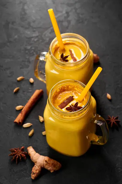 Photo of Hadi Doodh know as Golden Turmeric Milk in Mason Jar on black slate background. Golden Milk is ayurvedic recipe of hot milk with turmeric, ginger and spices.