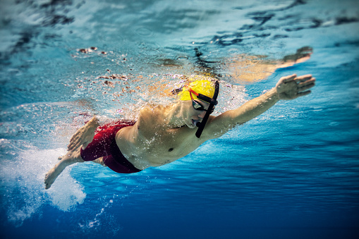 Underwater shot of young man practicing front crawl style of swimming in the swimming pool. Photo taken from low angle
