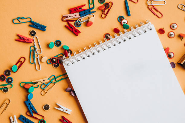 istock Office supplies of colored buttons and paper clips with empty note pad with copy space on yellow background 1210371861