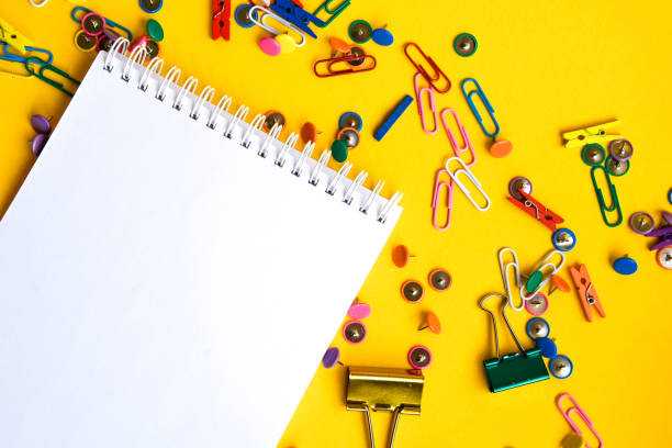 istock Office supplies of colored buttons and paper clips with empty note pad with copy space on yellow background 1210371881