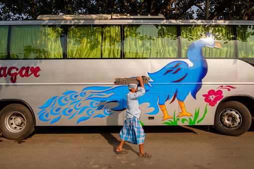 Kolkata, India - May 11, 2017: A man carries goods on his head while walking by a bus with a large bird painted on it at the Esplanade Bus Terminus by Kolkata’s New Market.