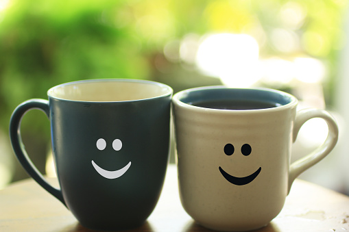 Two cups of tea or coffee closeup with smiling faces emoticon on it. Cheer up your day with a smile concept with blue and white couple cup. Copy space for your text or design background.