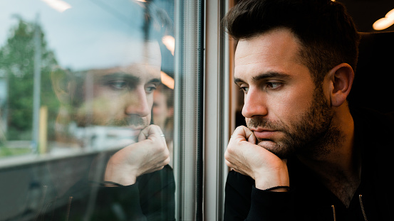 Young bearded man traveling by train in late afternoon