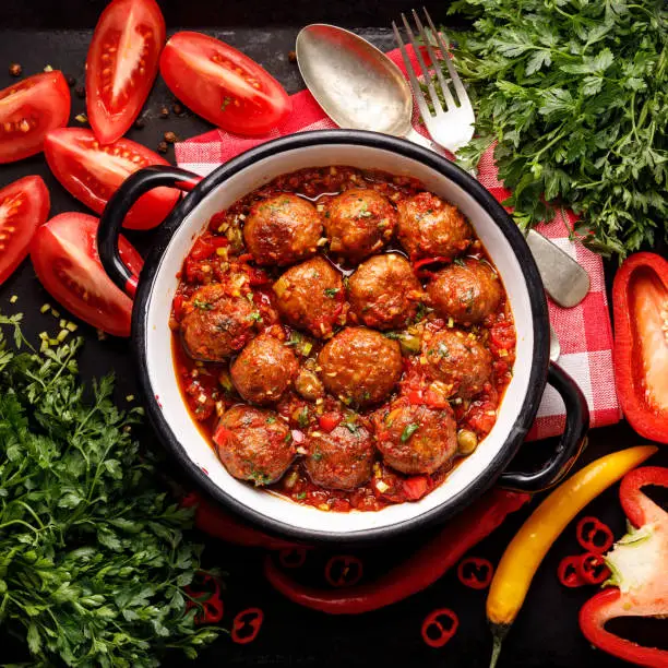 Meatballs in tomato sauce with the addition of aromatic herbs in an enamel dish top view