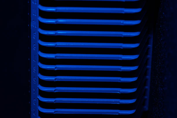 Close-up of stacked turquoise folding metal chairs and round tables against a light wall. Repetition and symmetry in urban outdoor furniture storage.
