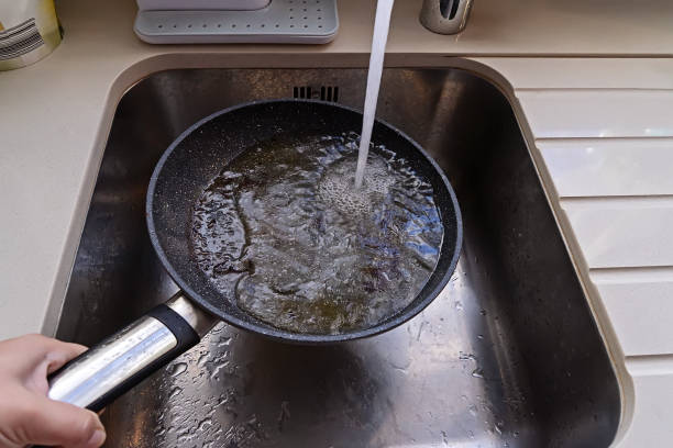 frying pan with non-stick surface and hot oil under water tap flow in sink - yan imagens e fotografias de stock