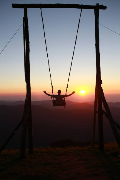 Silhouette of man swinging on a swing at sunset. back view
