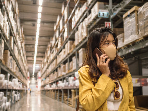 istock Woman wearing a face mask and using smartphone in warehouse. 1210394034