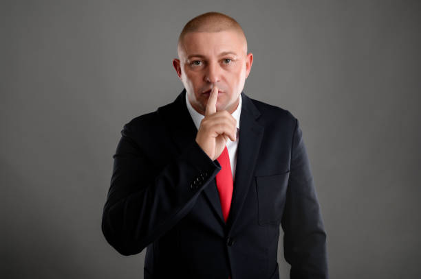istock Businessman dressed in black suit placing fingers on lips as if 1210409202