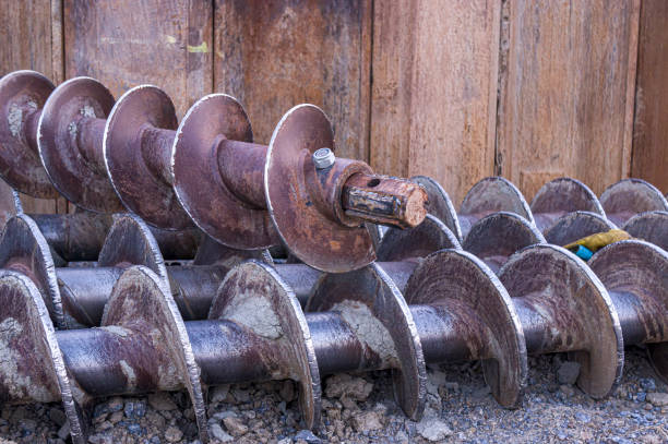 Building site with gravel, shovel, metal beams and an auger behind a fence
