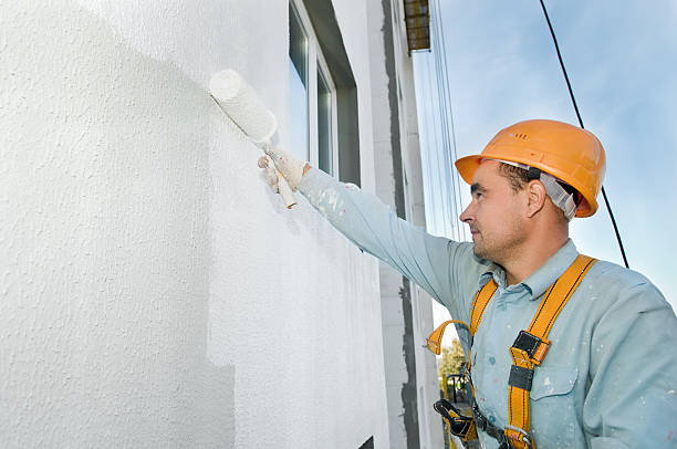 A builder painting a wall while wearing safety gear