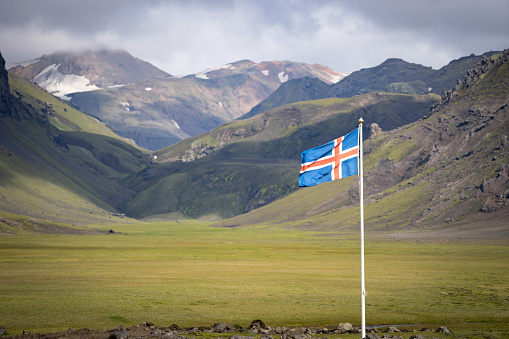Flag of Iceland against the background of green mountains and blue sky.