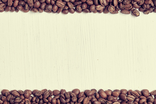 Coffee beans are scattered in line on a white wooden background. Toned. Close up.