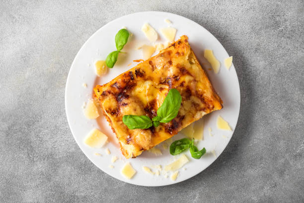 lasaña de carne casera con albahaca fresca y queso parmesano en un plato sobre fondo de hormigón gris. vista superior - lasaña fotografías e imágenes de stock