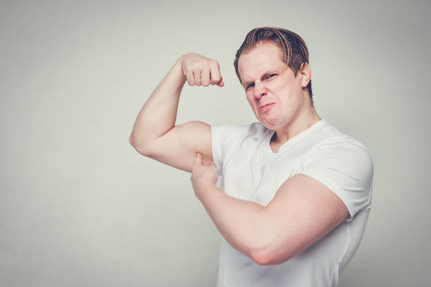 istock A man in a white T-shirt jokingly poses and points to his biceps. Toned. 1210420594