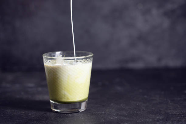 istock Green matcha latte with pouring milk on a black background with copy spase 1210430436