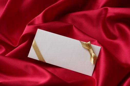 High angle view of blank envelope with decorated gold ribbon on red satin.