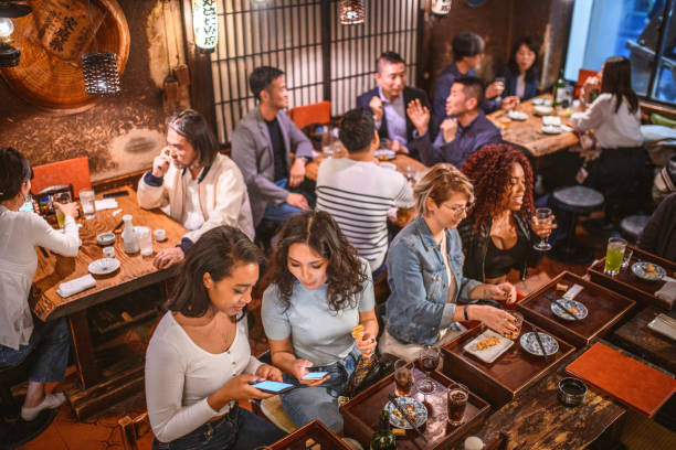 High Angle View of Male and Female Patrons at Tokyo Izakaya Wide angle view of multi-ethnic clientele of diverse ages enjoying drinks and food at Tokyo izakaya. central asian ethnicity stock pictures, royalty-free photos & images