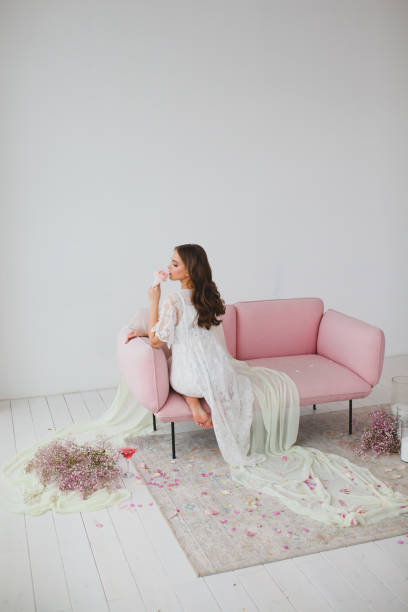 istock Young bride in white negligee posing on the rose sofa in the studio 1210441674