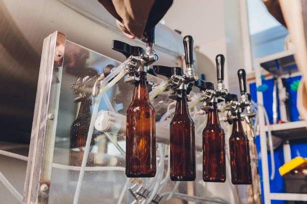 пивоваренный завод разливает пиво в стеклянные бутылки на конвейерных линиях. промышленная работа, автоматизированное производство проду - bottling plant brewery industry food стоковые фото и изображения