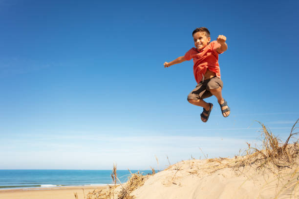 istock Happy little boy jump high on the sand beach 1210442082