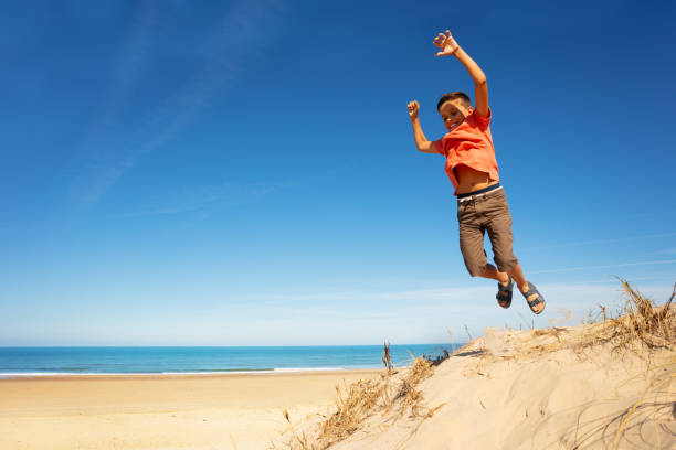 istock Boy jumps from sand dune on a beach rising hands 1210442083