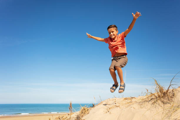 istock Cute boy jump on the sand dune beach with hands up 1210442097