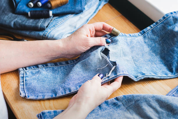 A woman is repairing ripped blue jeans. The concept of economical reuse of things. Homemade needlework. A woman is repairing ripped blue jeans. The concept of economical reuse of things. Homemade needlework. Horizontal frame selective focus hole in pants stock pictures, royalty-free photos & images