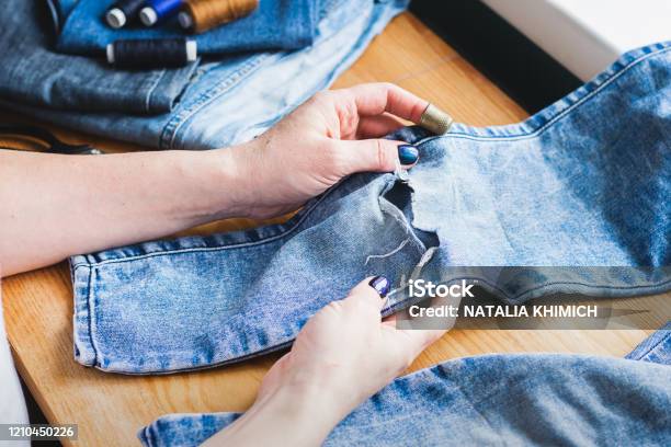 A Woman Is Repairing Ripped Blue Jeans The Concept Of Economical Reuse Of Things Homemade Needlework Stock Photo - Download Image Now