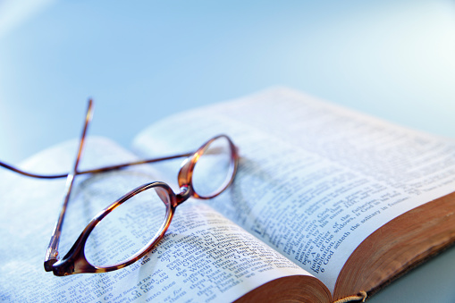 A pair of eyeglasses rest upside down on top of an open Holy Bible.