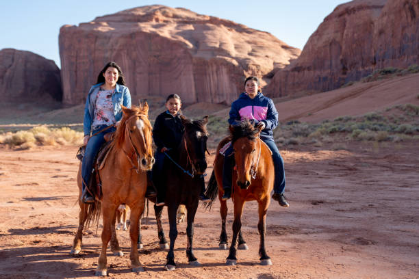 junge navajo teenage geschwister auf ihren pferden mit einer felsformation hinter ihnen - monument valley navajo mesa monument valley tribal park stock-fotos und bilder