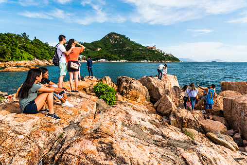 Hong Kong- July 27, 2019: People have rest on the rocks of Stanley Bay shore in Hong Kong. Beautiful scenic sunset landscape with water, mountains, rocks, and buildings.