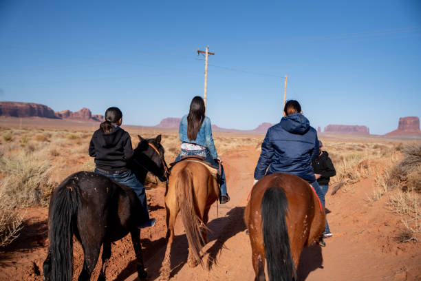junge navajo teenage geschwister auf ihren pferden mit einer felsformation hinter ihnen - monument valley navajo mesa monument valley tribal park stock-fotos und bilder