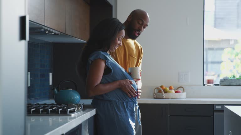 Loving Hispanic Husband With Pregnant Wife At Home In Kitchen Feeling Baby Kick Together