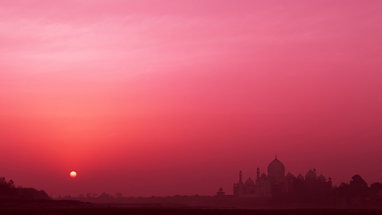 Silhouette of majestic ancient Taj Mahal temple at sunrise; UNESCO world heritage, bank of the Yamuna river in Agra, India