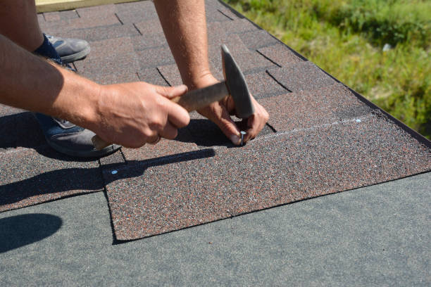 Roofer installing Asphalt Shingles on a house construction roof corner with a hammer and nails. Roofing construction with Asphalt Shingles.