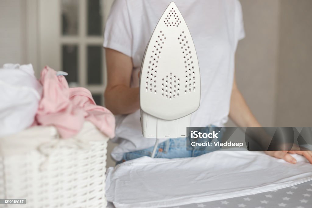 Woman holds modern styled iron with non-stick cover while ironing Woman holds modern styled iron with non-stick cover while ironing. Iron - Appliance Stock Photo
