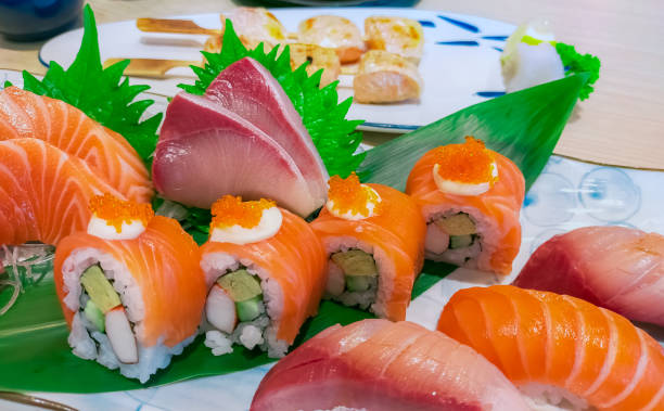 combinazione di cibo giapponese impostata su piatto bianco. sushi di salmone, sashimi e nigiri sul tavolo del ristorante. carne di pesce affettata e involtini di riso aceto giapponesi con frutti di mare e verdure. cibo giapponese sano. - japanese cuisine temaki sashimi sushi foto e immagini stock