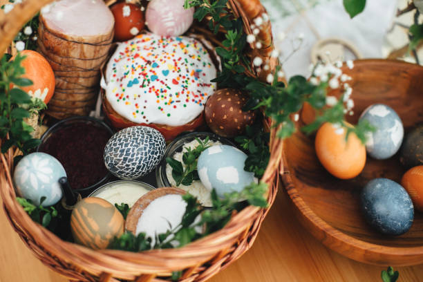 istock Easter modern eggs, easter bread, ham, beets, butter, in wicker basket decorated with green buxus branches and flowers on rustic wooden table. Traditional Easter basket. 1210486681