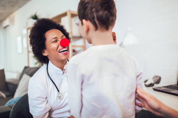 kinderarzt mit stethoskop im gespräch mit kleinem jungen - clownsnase stock-fotos und bilder